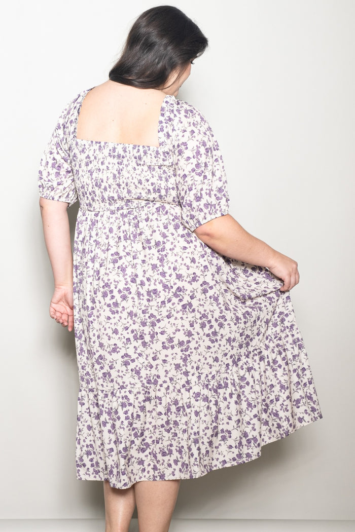 woman wearing a plus-size cream and purple floral print dress with a smocked back and puff sleeves
