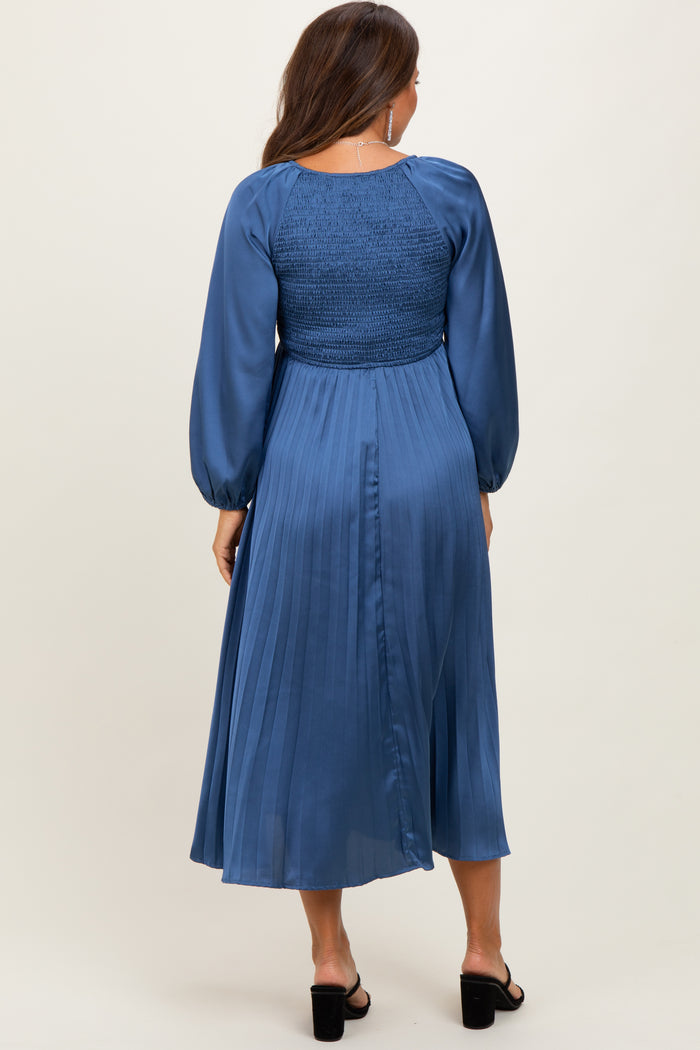 woman wearing a blue pleated maternity dress with a smocked bodice and long puff sleeves, showing a baby bump