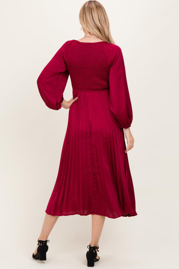woman wearing a burgundy long sleeve pleated dress with a smocked bodice and flowy skirt, shown from the back