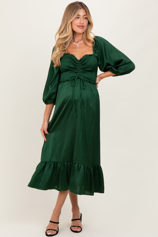 woman wearing a green maternity dress with a smocked bodice, puff sleeves, and a ruffled hem