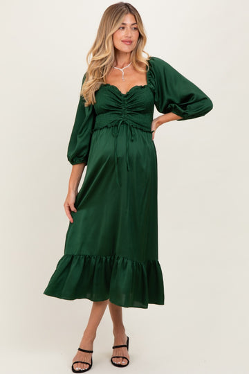 woman wearing a green maternity dress with a smocked bodice, puff sleeves, and a ruffled hem