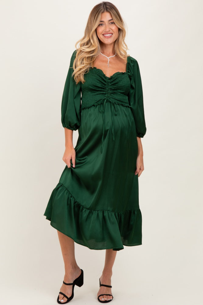 woman wearing a dark green maternity dress with a ruched bodice and ruffled hem, standing confidently