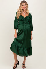 woman wearing a dark green maternity dress with a ruched bodice and ruffled hem, standing confidently