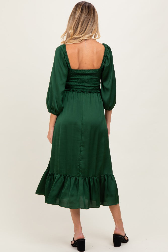 woman wearing a dark green maternity dress with a smocked bodice and puffed sleeves, showing a baby bump