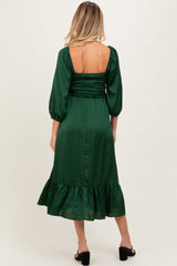 woman wearing a dark green maternity dress with a smocked bodice and puffed sleeves, showing a baby bump