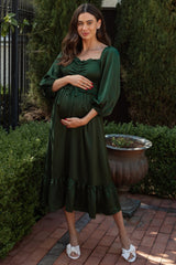 woman wearing a dark green maternity dress with puff sleeves and a ruffled hem, holding her baby bump