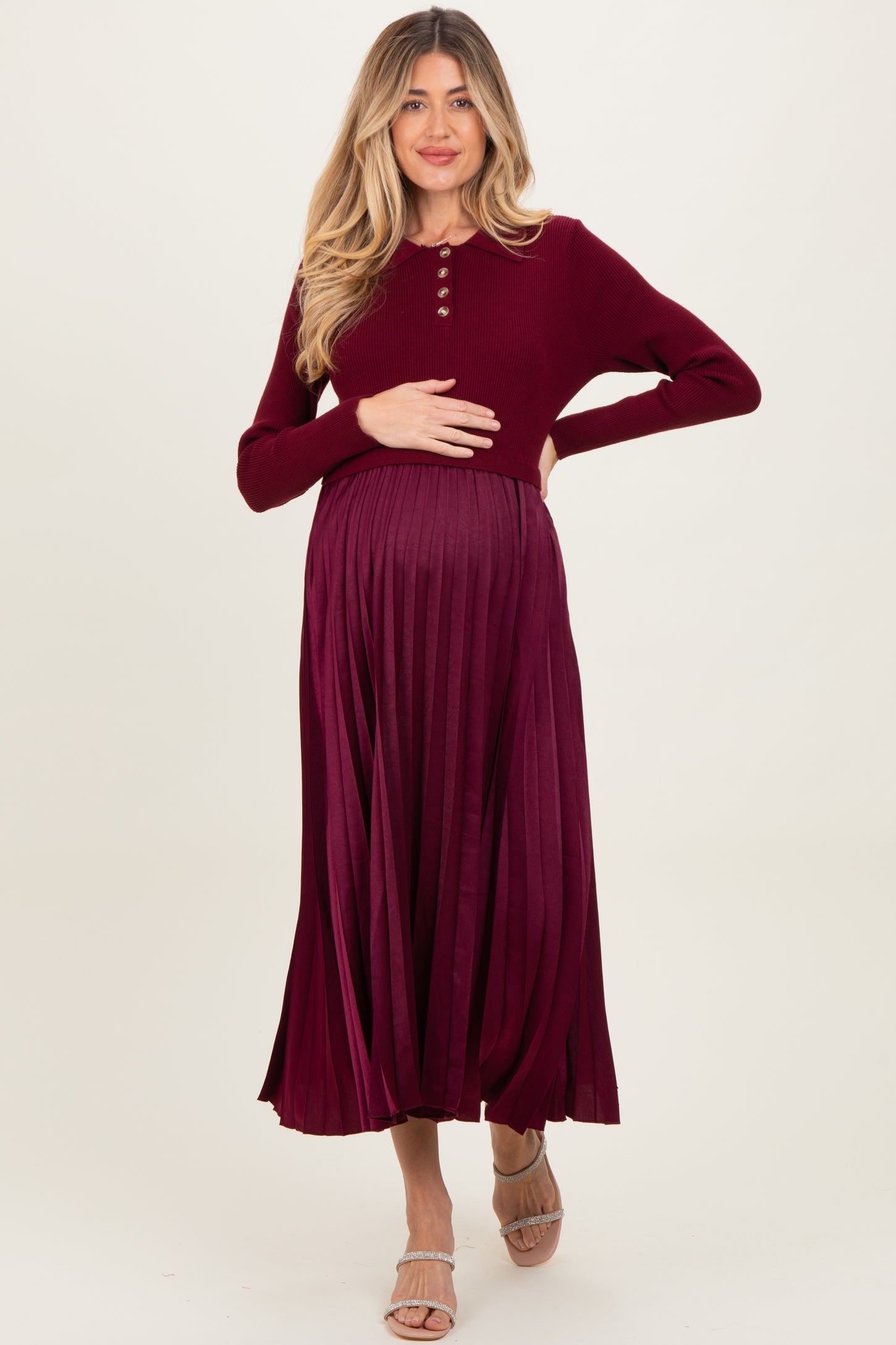 woman wearing a burgundy maternity dress with long sleeves and pleated skirt, holding her baby bump