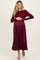 woman wearing a burgundy maternity dress with long sleeves and pleated skirt, holding her baby bump