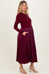woman wearing a burgundy maternity dress with a buttoned collar and pleated skirt, showing her baby bump