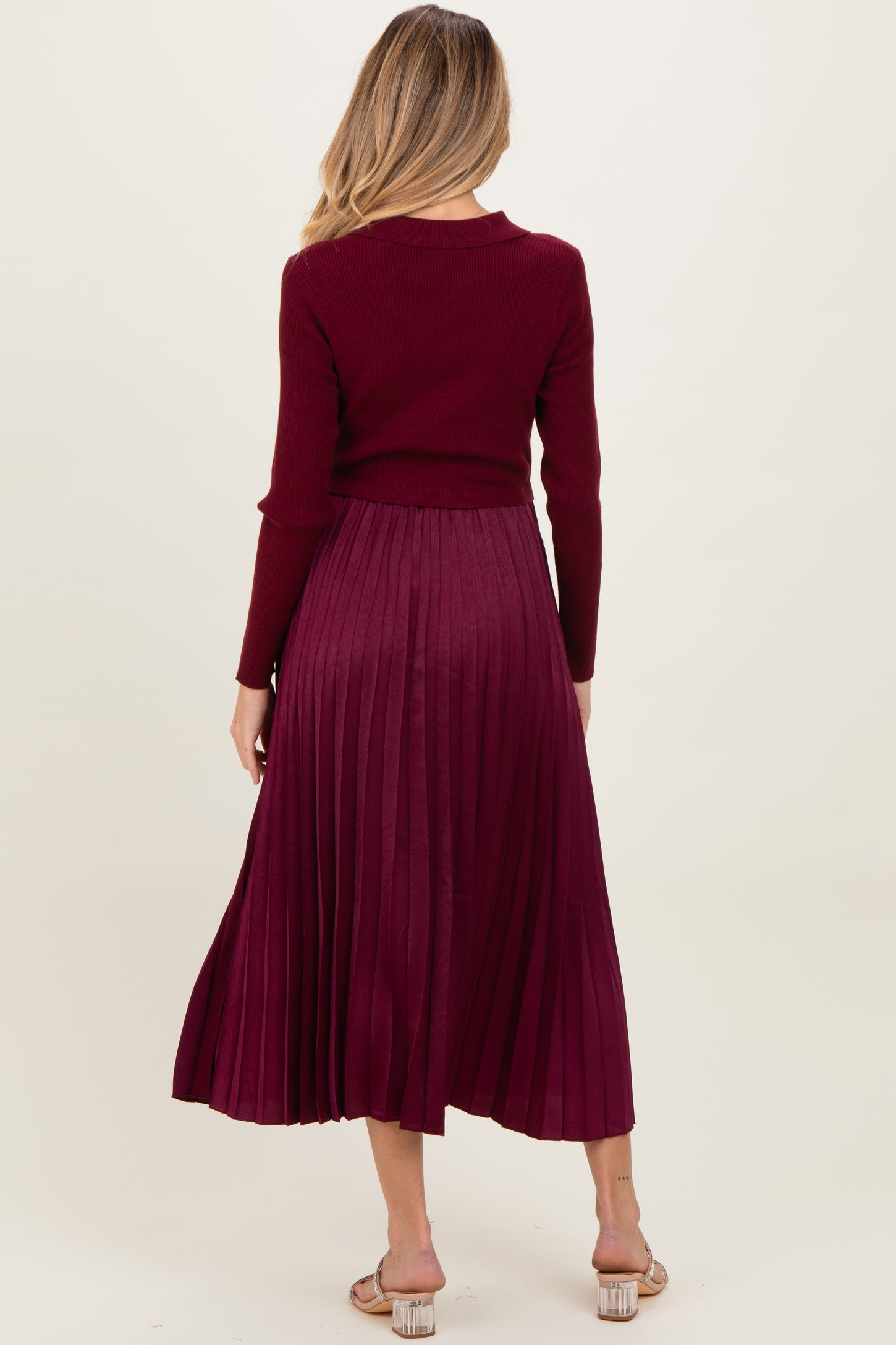 woman wearing a burgundy maternity sweater and pleated maxi skirt, showing a visible baby bump from behind