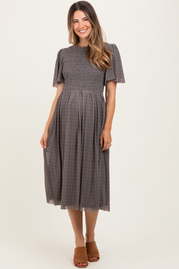 woman wearing a brown plaid maternity dress with short puff sleeves and a smocked bodice, showcasing her baby bump