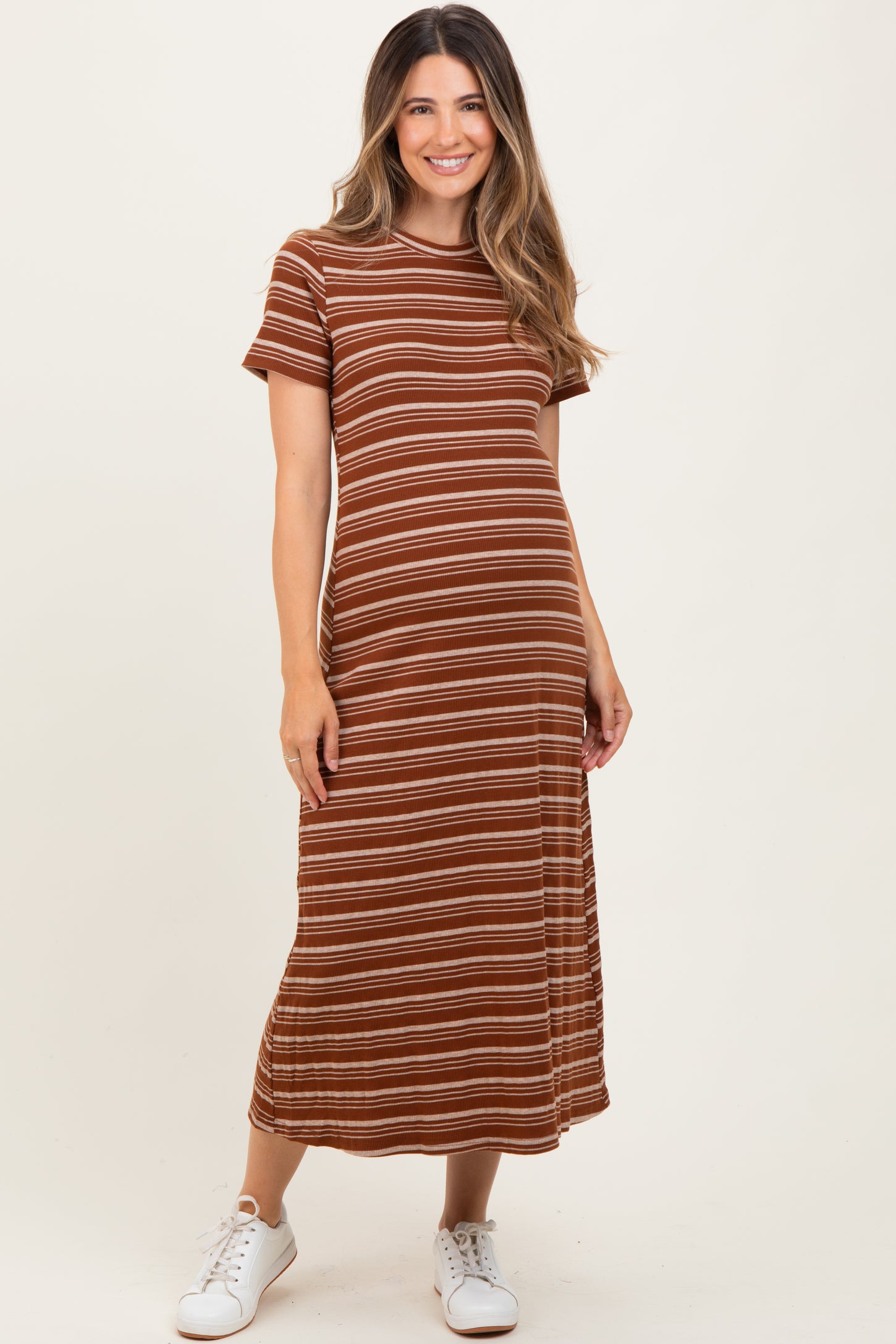 woman wearing a brown striped maternity dress with short sleeves and a fitted silhouette, paired with white sneakers