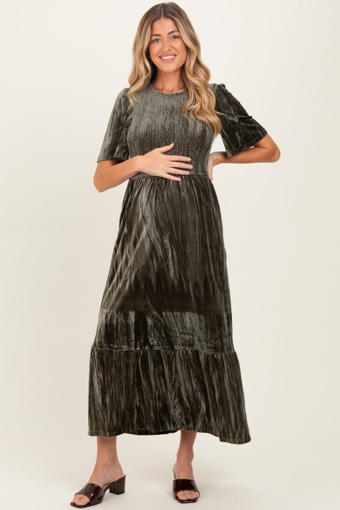 woman wearing a dark green velvet maternity dress with smocked bodice and tiered hemline, holding her baby bump
