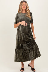 woman wearing a dark green velvet maternity dress with short sleeves and a tiered skirt, holding her baby bump