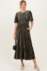 woman wearing a dark green smocked velvet maxi dress with short puff sleeves and a tiered skirt, holding a small handbag