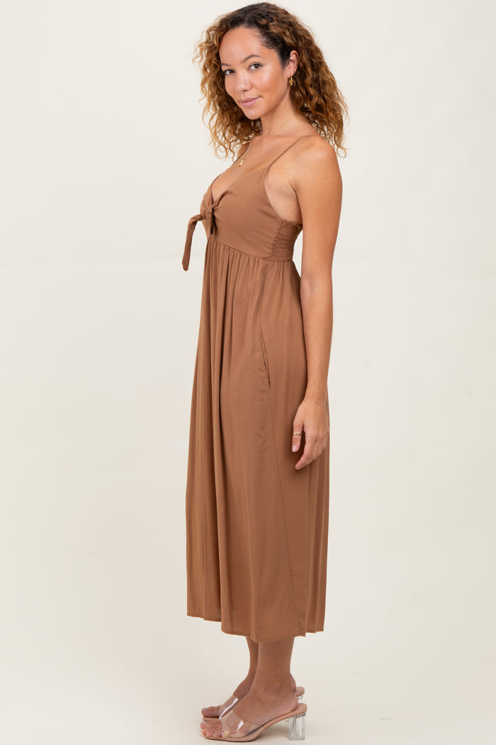 woman wearing a brown sleeveless maxi dress with a tie detail at the bust and side pockets