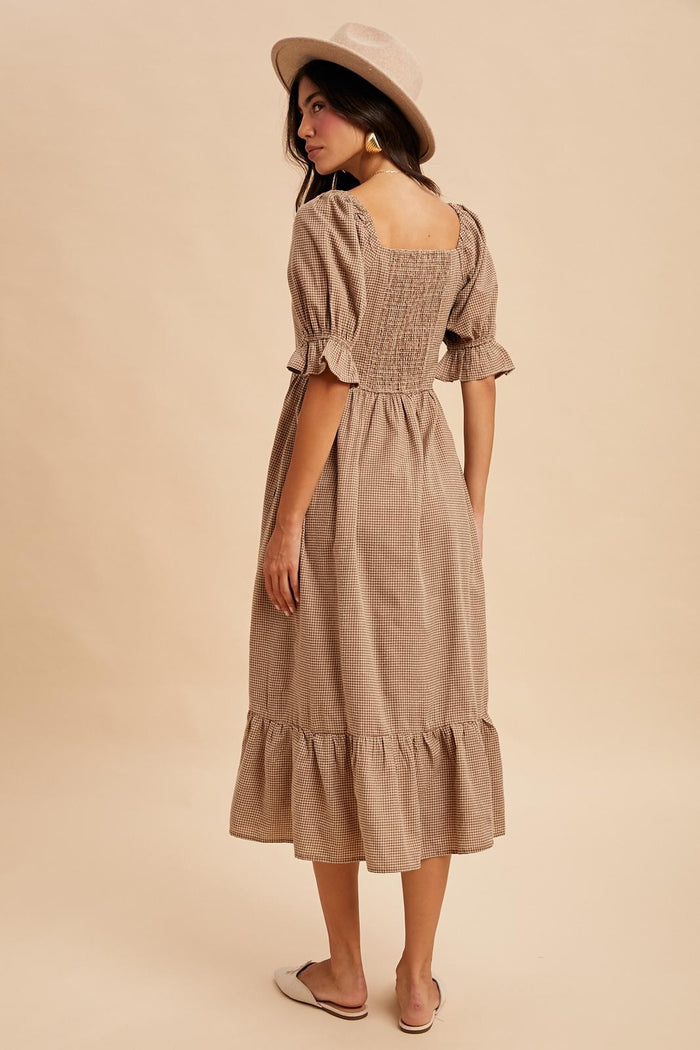 woman wearing a beige gingham midi dress with puff sleeves and a ruffled hem, paired with a stylish hat