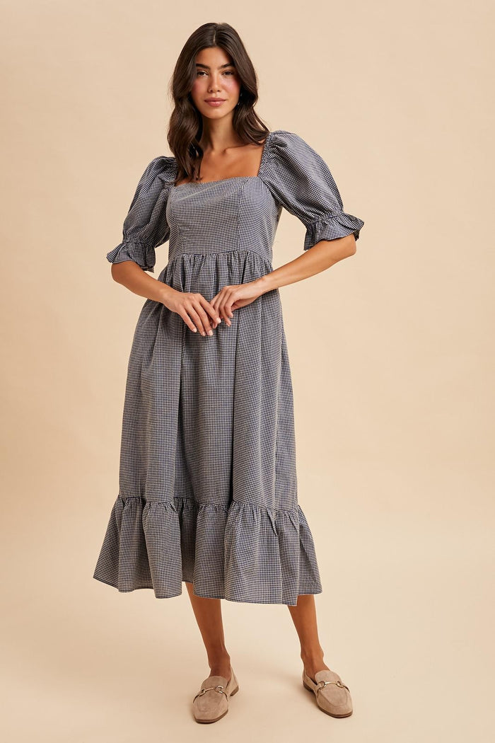 woman wearing a blue and white gingham midi dress with puff sleeves and a tiered hem