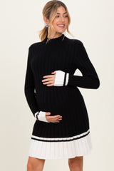 woman wearing a black and white ribbed maternity dress with long sleeves and pleated hem while holding her baby bump