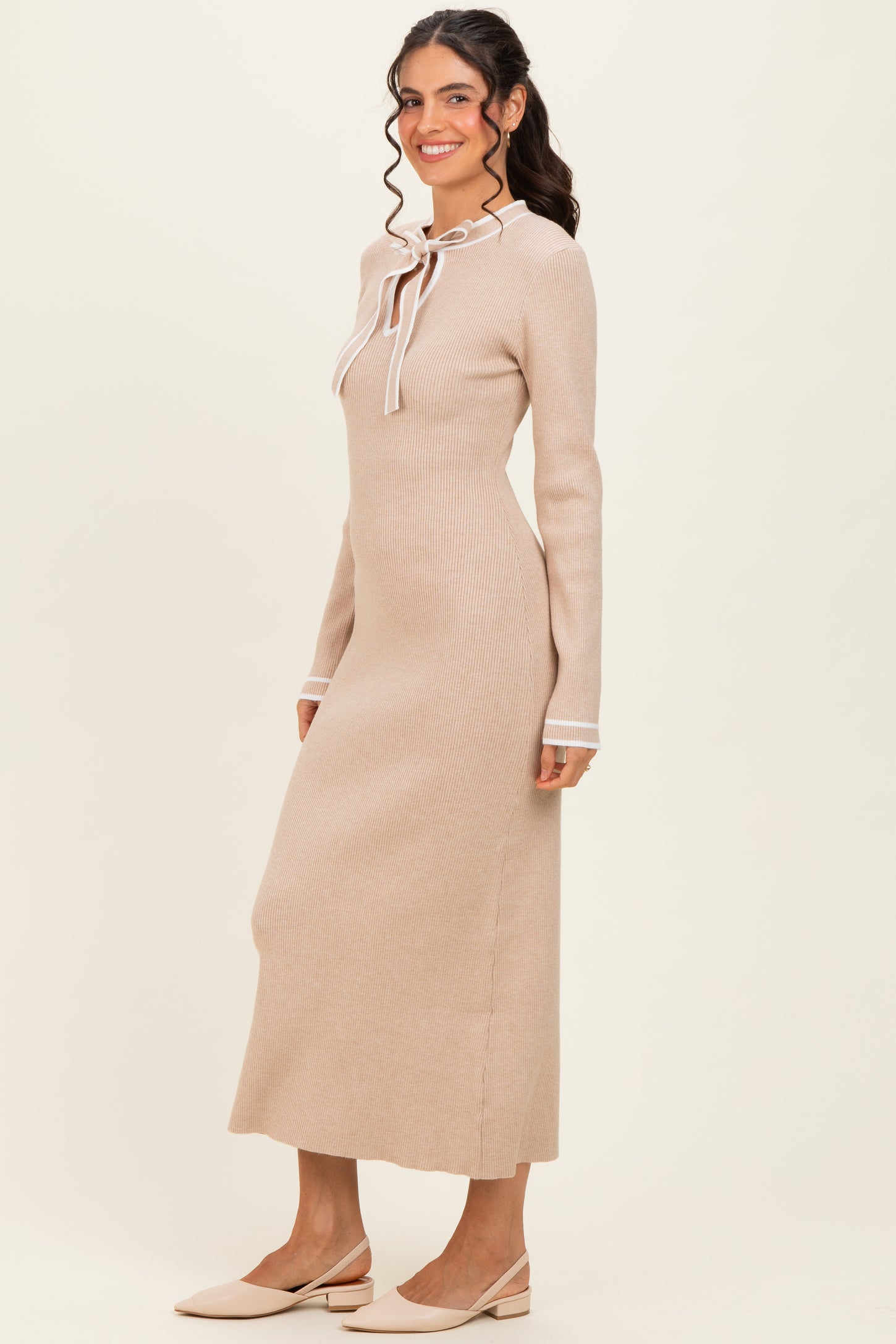 woman wearing a beige long sleeve ribbed maxi dress with a tie neck detail and white trim