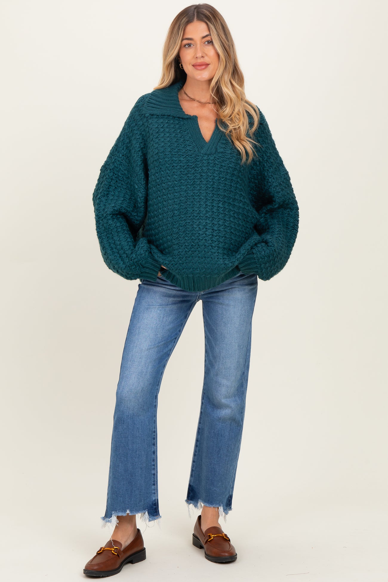 woman wearing a teal maternity sweater with a collar and loose sleeves paired with frayed hem jeans.
