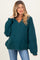 woman wearing a dark teal oversized knitted maternity sweater with a v-neck and relaxed fit, showing a baby bump