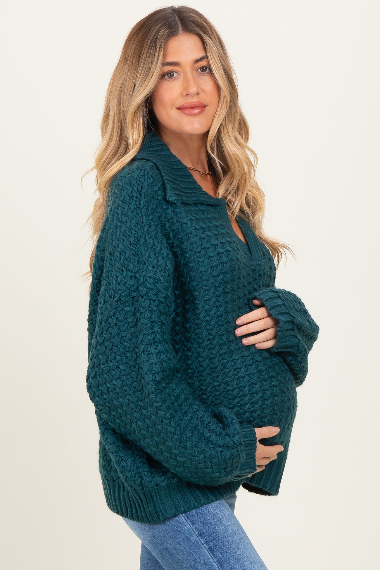 woman wearing a dark green chunky knit maternity sweater and holding her baby bump