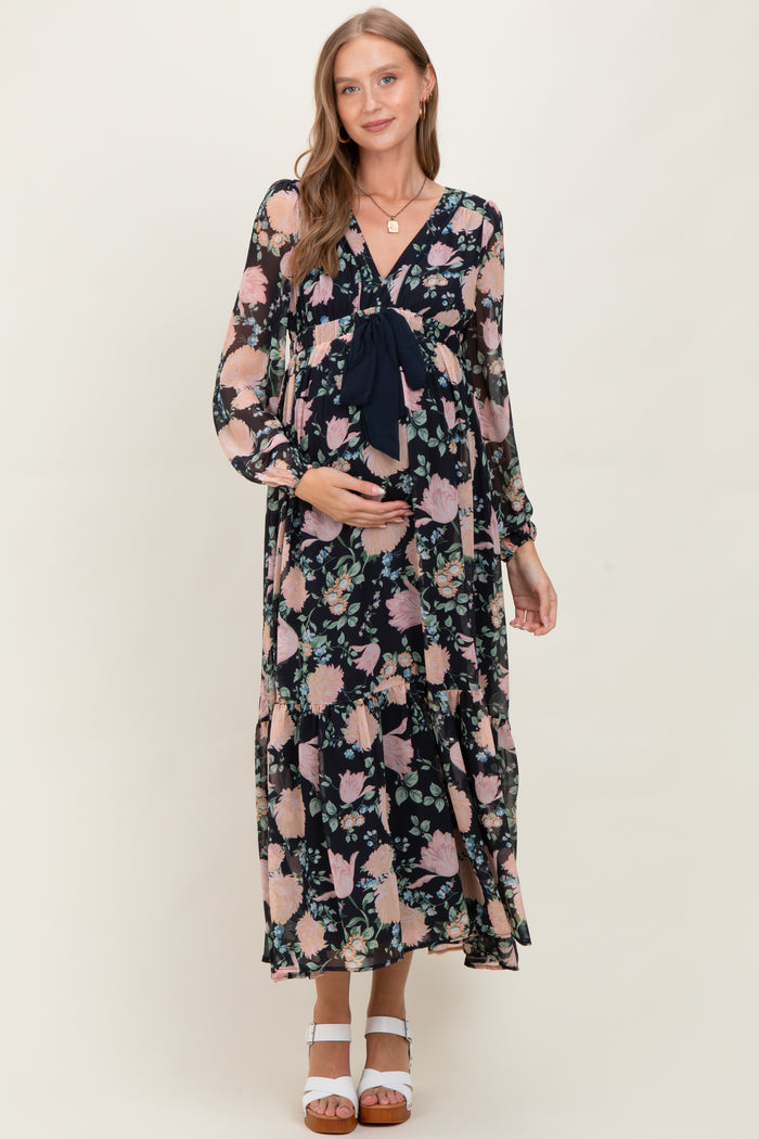 woman wearing a floral maternity maxi dress with a tie at the bust, holding her baby bump