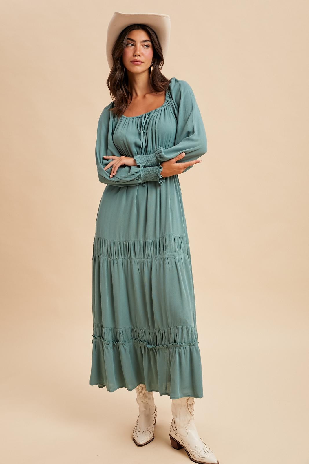 woman wearing a teal long sleeve tiered maxi dress and white cowboy boots with a wide-brimmed hat