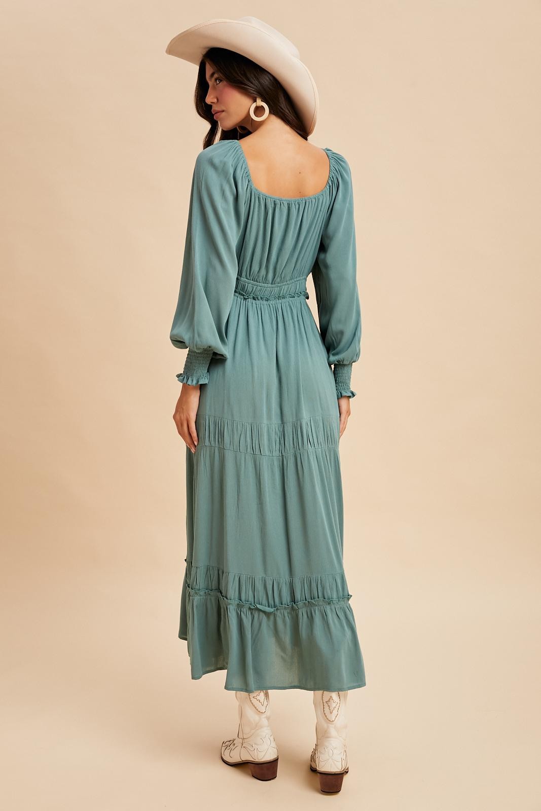 woman wearing a teal long sleeve tiered maxi dress with a smocked waist and white cowboy boots, facing away from the camera