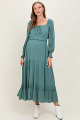 woman wearing a dusty teal maternity dress with long sleeves and tiered ruffle details, featuring a tied neckline