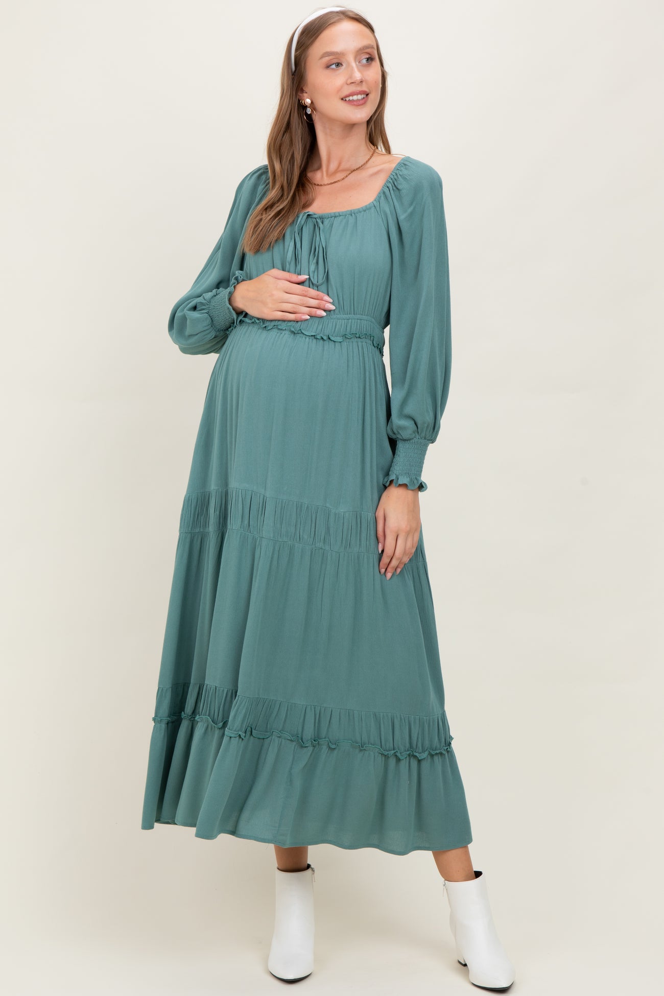 woman wearing a jade green maternity maxi dress with puff sleeves and a cinched waist, highlighting her baby bump