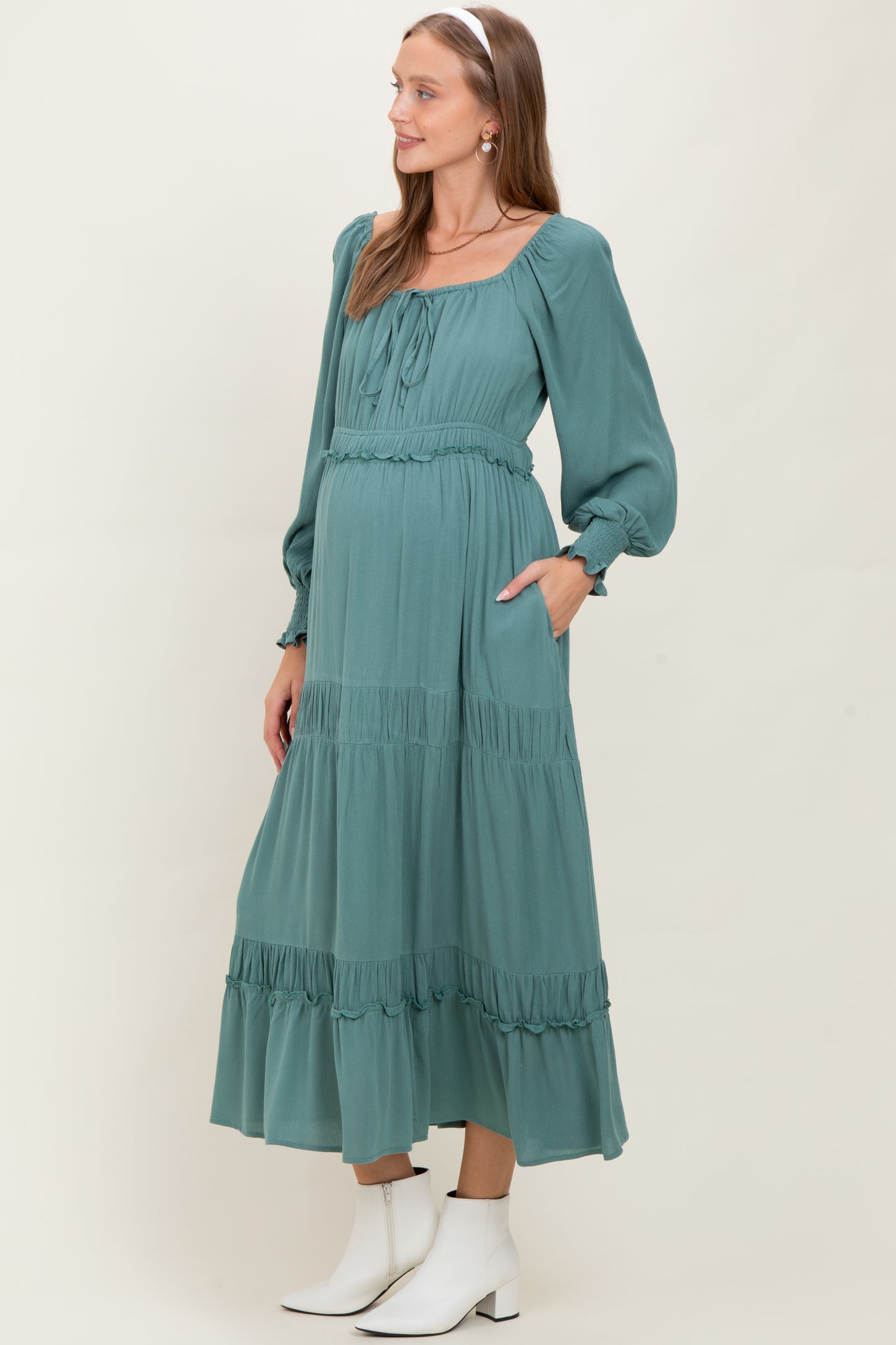 woman wearing a teal maternity maxi dress with long sleeves, ruffle details, and a visible baby bump