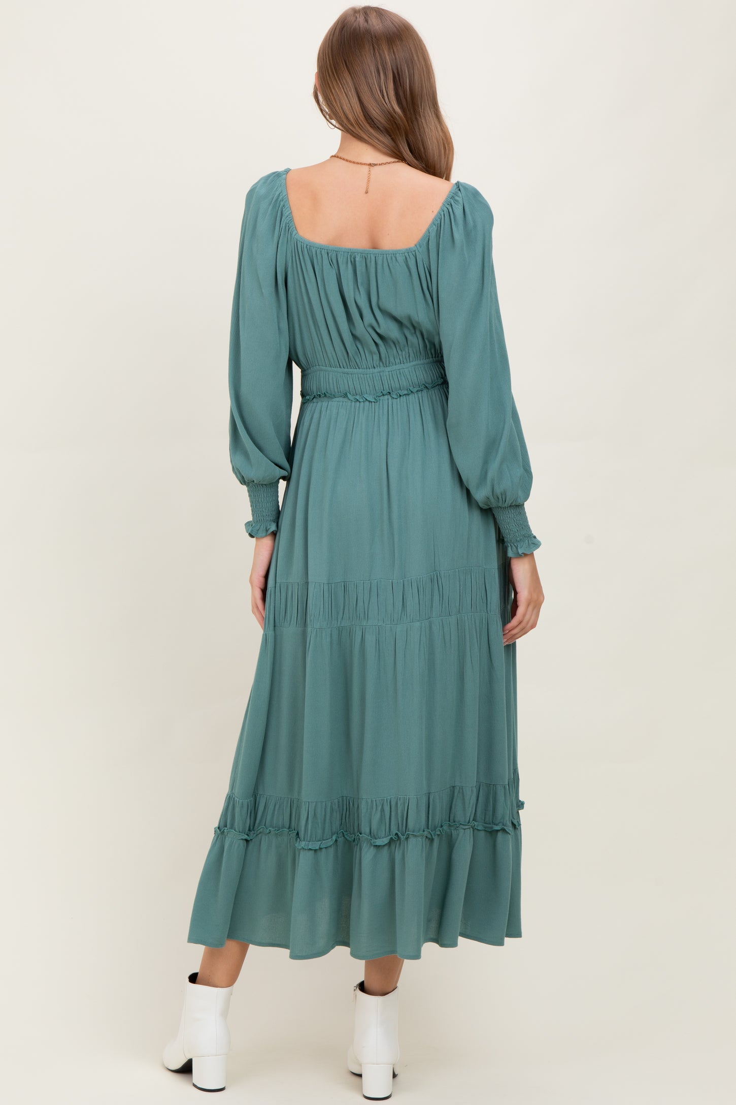 woman wearing a teal long sleeve maternity dress with a smocked waist and tiered ruffle hem, showing a baby bump
