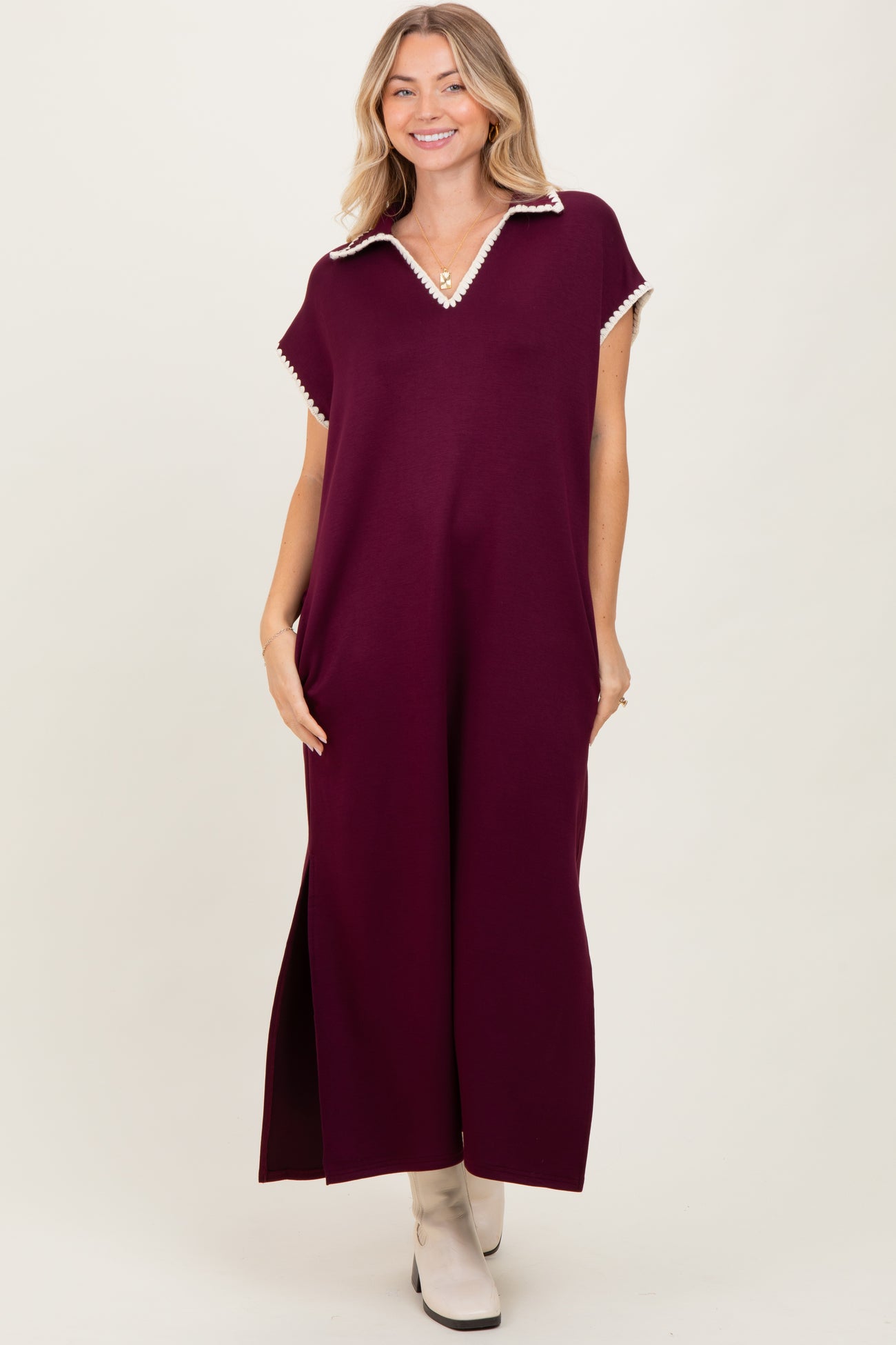 woman wearing a burgundy maxi dress with a collar and decorative trim, standing with a relaxed fit and side slits