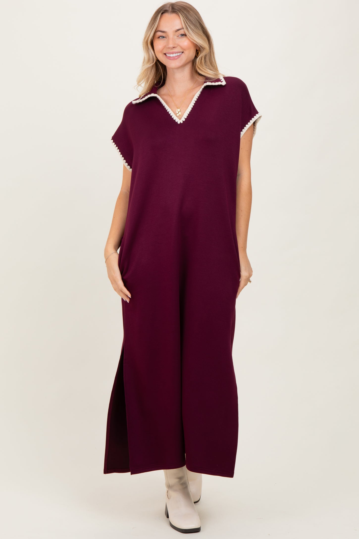 woman wearing a burgundy maxi dress with a collar and decorative trim, standing with a relaxed fit and side slits