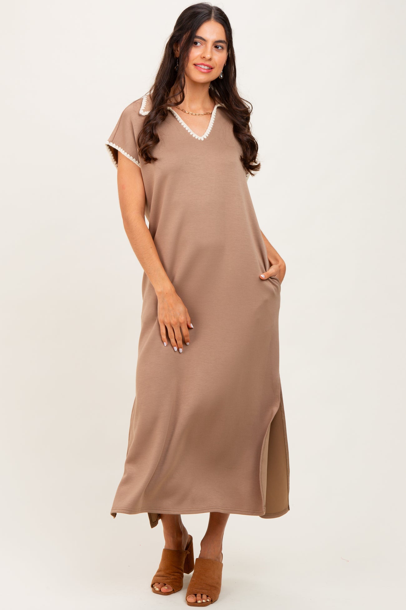 woman wearing a taupe maxi dress with a v-neck and short sleeves, featuring a lace trim and side slits