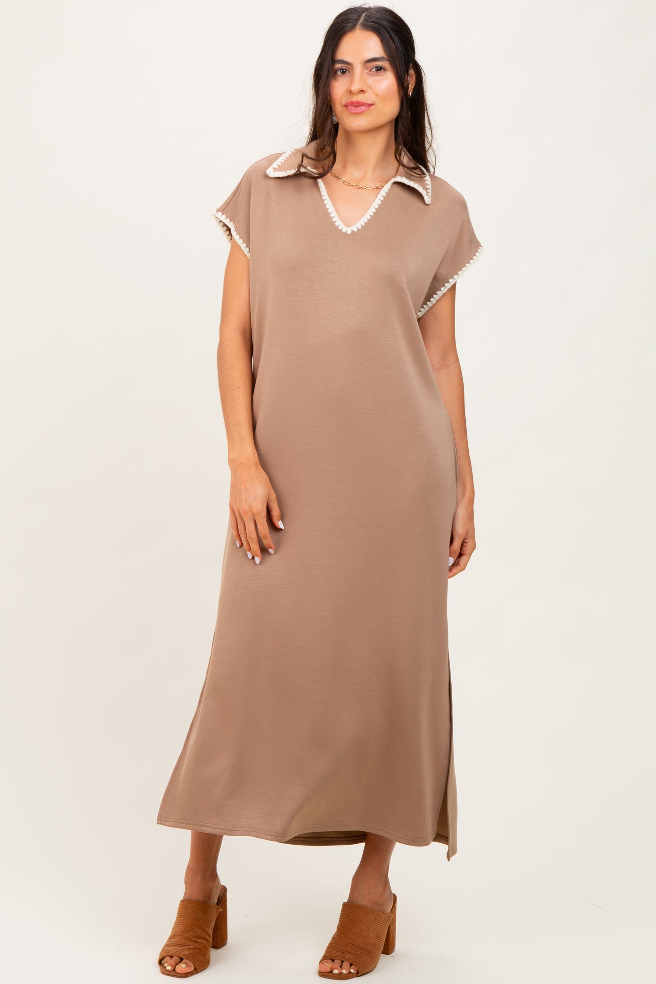 woman wearing a brown maxi dress with a white collared neckline and side slits, standing and smiling