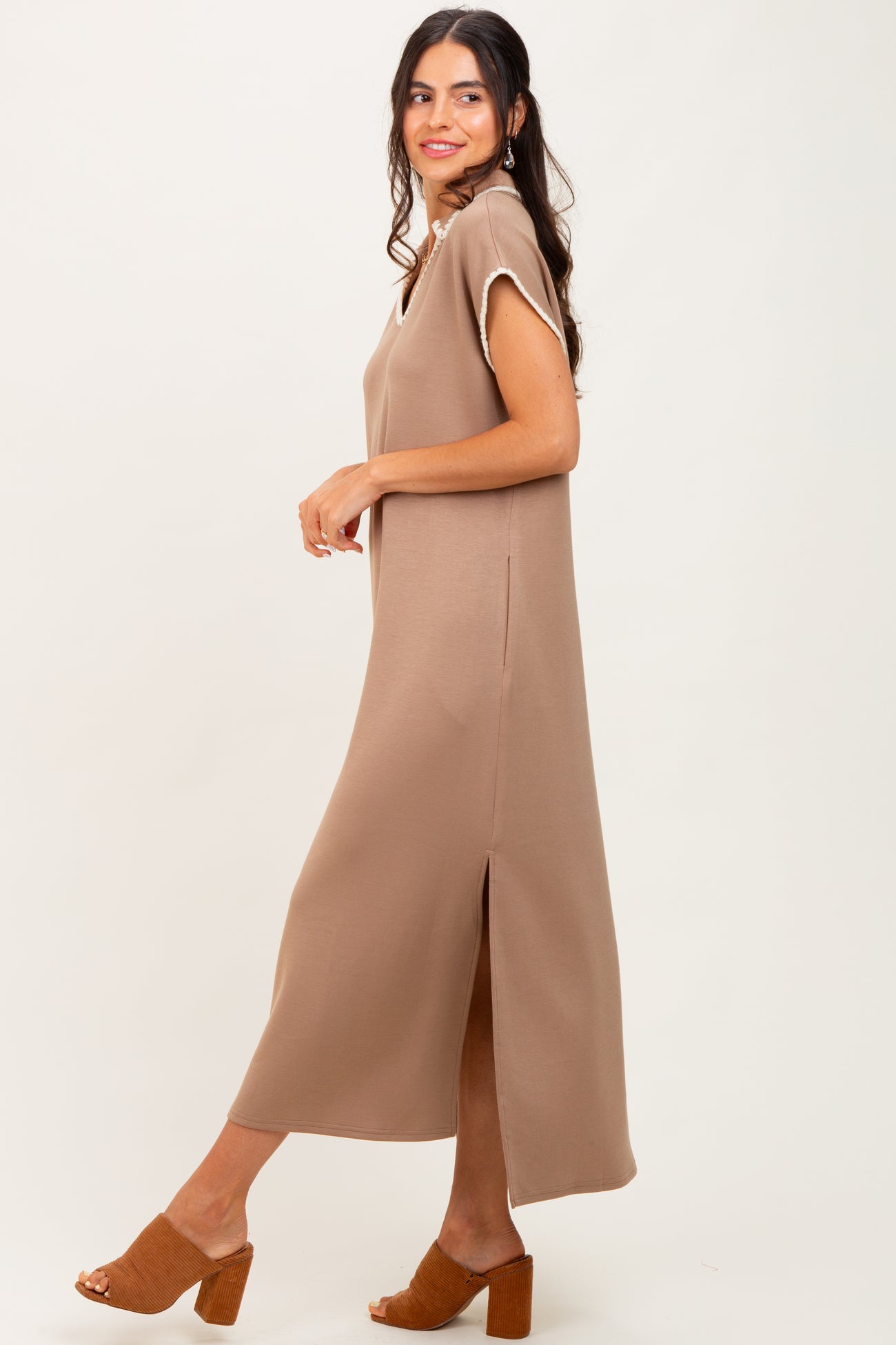 woman wearing a brown sleeveless maxi dress with side slits and a relaxed fit, standing sideways on a light background