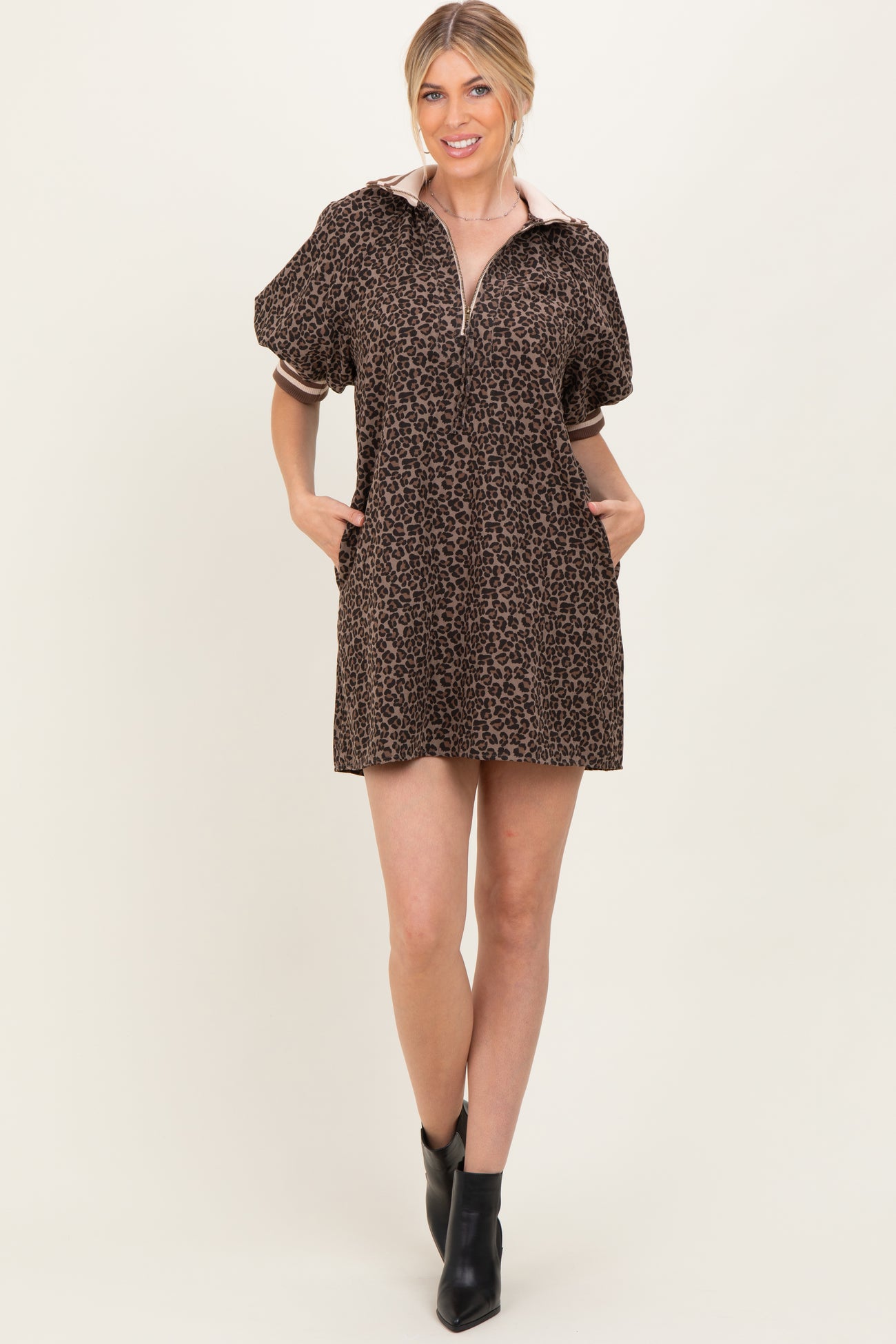 woman wearing a brown leopard print short dress with a zip-up collar and puff sleeves, standing with hands in pockets