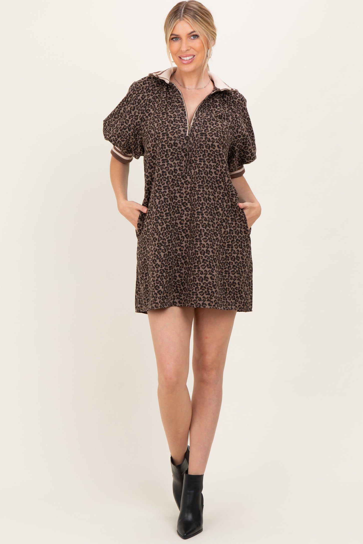 woman wearing a brown leopard print short dress with a zip-up collar and puff sleeves, standing with hands in pockets