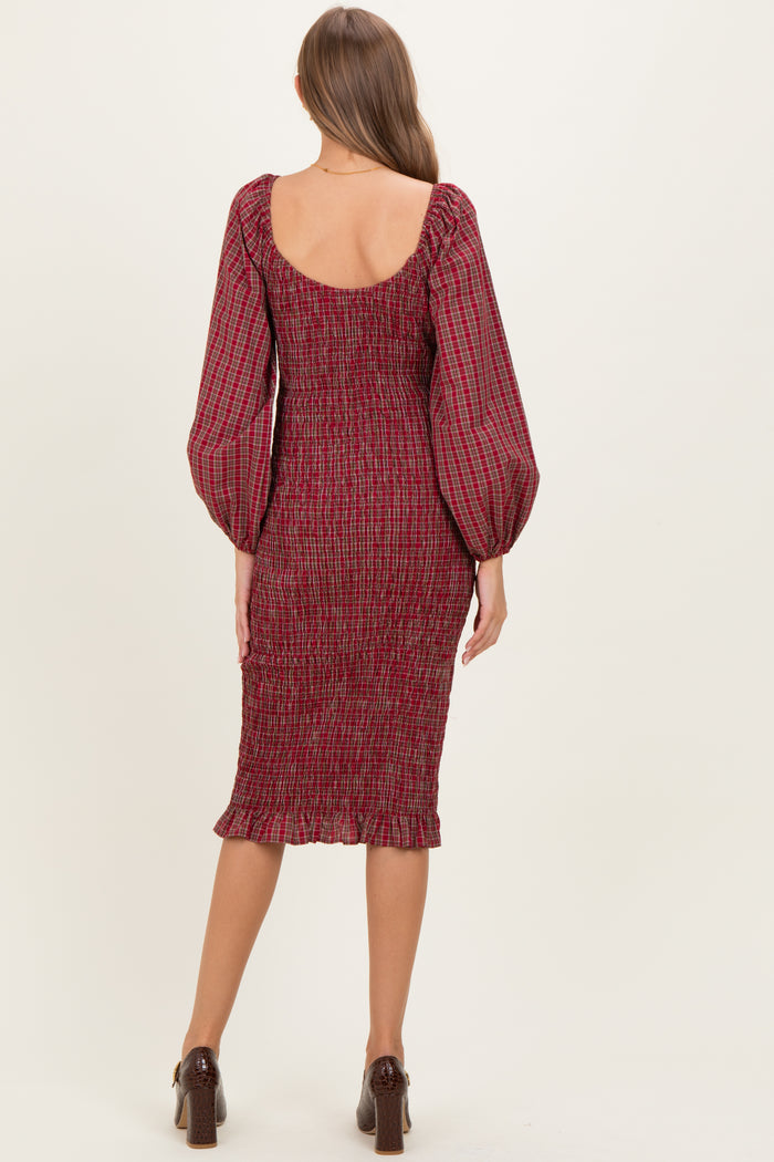 woman wearing a burgundy smocked maternity dress with long puffed sleeves and a midi length