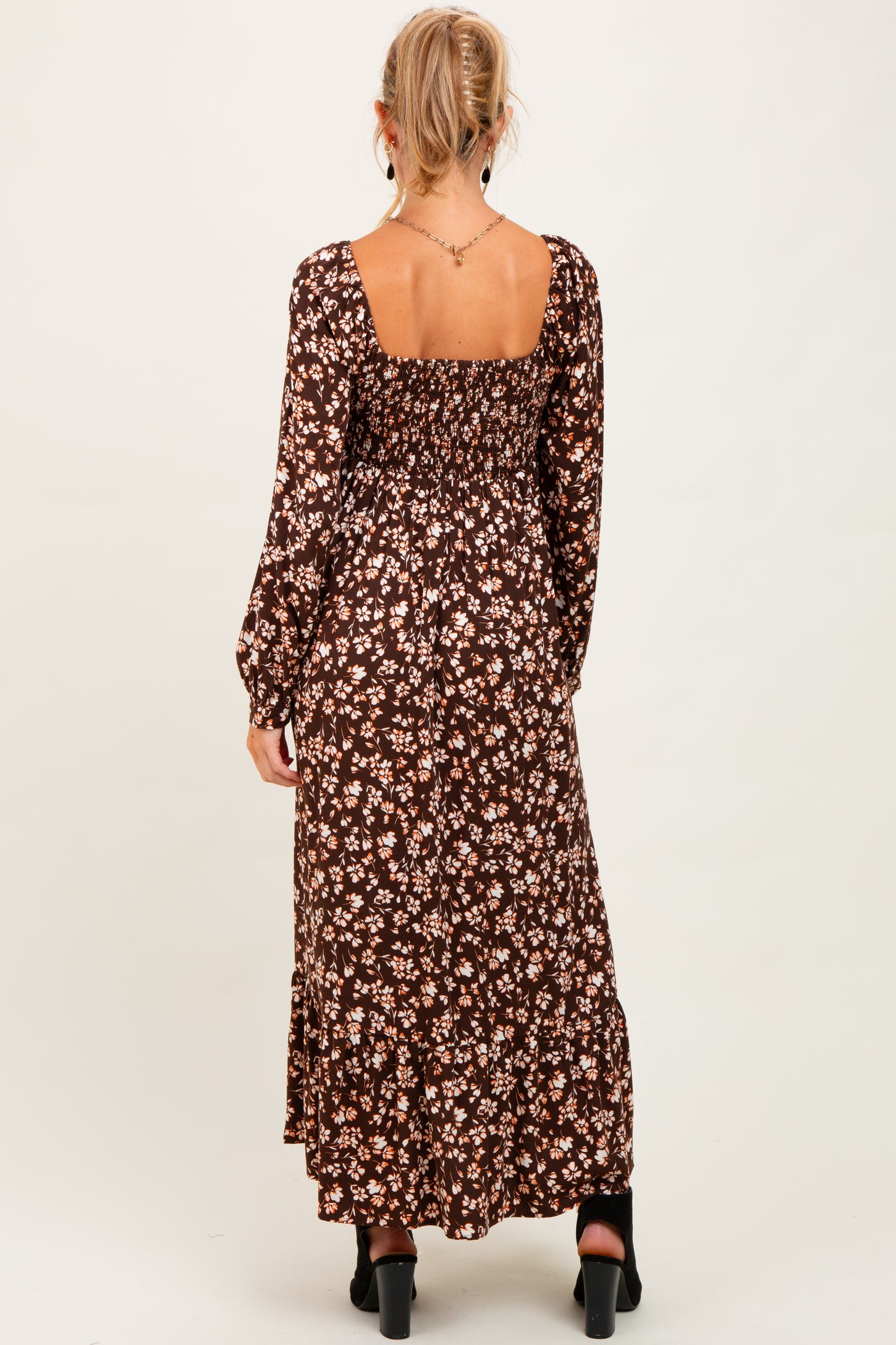 woman wearing a brown floral maternity maxi dress with long sleeves and a smocked back, model seen from the back