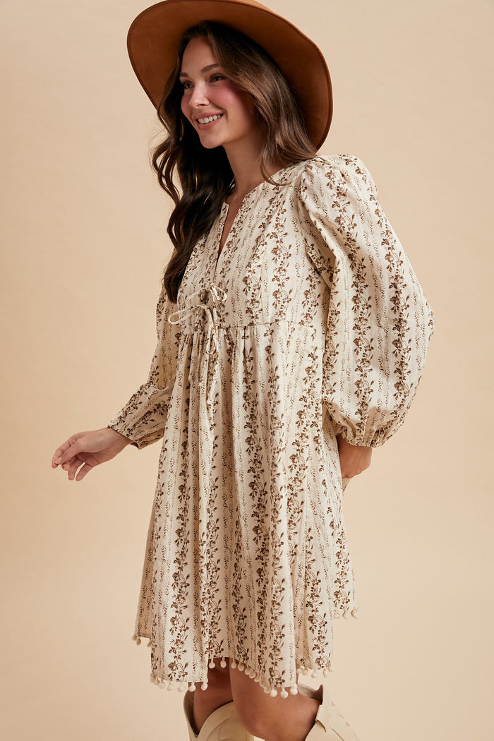 woman wearing a cream floral print puff sleeve dress with a drawstring waist and a wide-brimmed hat