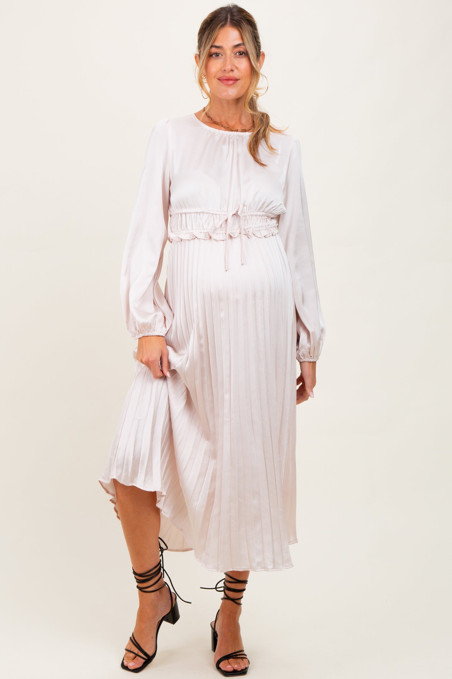 woman wearing a blush satin maternity dress with pleats and long sleeves, showing her baby bump