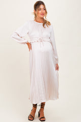 woman wearing a light pink pleated maternity dress with long sleeves and a gathered waist, showing her baby bump