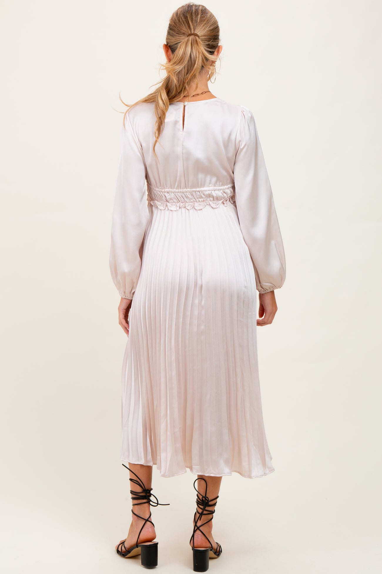 woman wearing a light pink satin maternity dress with a pleated skirt and elastic waist, showing her baby bump from the back