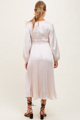 woman wearing a light pink satin maternity dress with a pleated skirt and elastic waist, showing her baby bump from the back