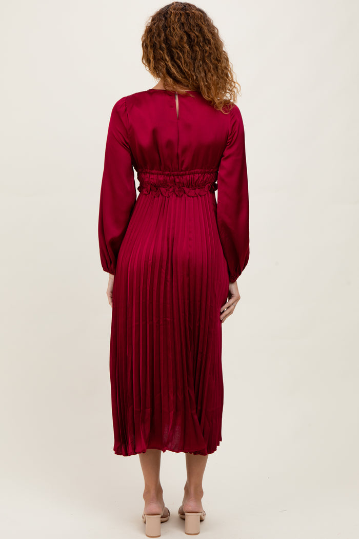 woman wearing a burgundy midi dress with pleated detailing and long sleeves, standing with her back to the camera