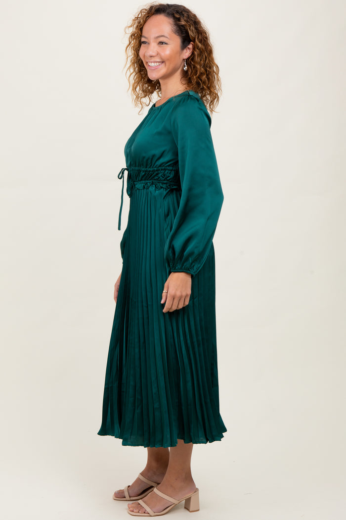 woman wearing a dark green pleated long sleeve dress with a drawstring waist and soft sheen finish